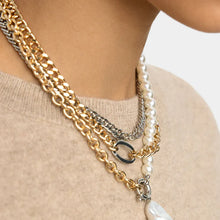 Close-up of layered necklaces with gold, silver, and pearl chains on a neutral background.