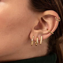 Close-up of an ear with gold hoop earrings on a blurred background
