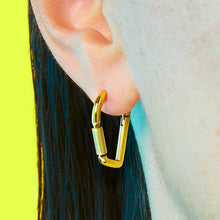 Close up of a person wearing a gold carabiner earring