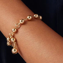 Gold beaded bracelet on a wrist against a dark background